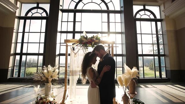 Newlywed couple touching foreheads at wedding alter, beautiful venue bright sunshine. HD 24FPS.