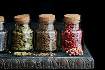spices in bottles, variety of different spices on the dark wooden table. pink pepper, cardamom, anise, black mustard seeds