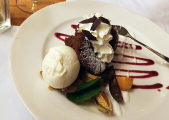 Chocolate fudge brownie and vanilla ice cream scoops on top with chocolate sauce on white plate...