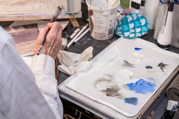 A senior hobby artist mixes paint on a palette and applies to canvas