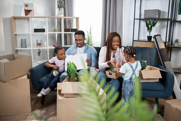 Obraz premium Young parents with kids playing on laptop and packing boxes