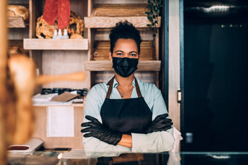 African American middle aged female worker with protective mask on face working in bakery....