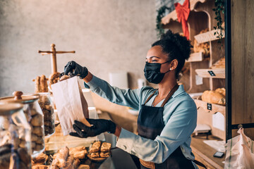 African American middle aged female worker with protective mask on face working in bakery. Coronavirus, Covid-19 concept.