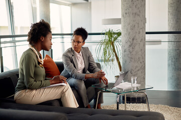 African American businesswoman uses laptop and coaching young assistant about the work in corporate...