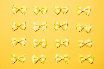 Yellow bow tie butterfly farfalle shape pasta pieces horizontally oriented pattern top view isolated on the bright solid yellow fond background
