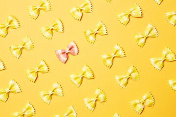 Pink bow tie butterfly farfalle shape pasta one alone single piece stands out of yellow pieces diagonally oriented pattern top view isolated on the bright solid yellow fond background