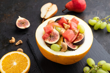 Vegetarian fruit salad of watermelon, grapes, figs, pear, orange, cashew  on black concrete background. Side view, close up.