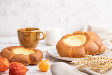 Sour cream bun with cup of coffee on a white wooden and concrete background. Side view, selective focus.