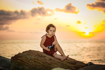 a little beautiful girl,on the beach,on a summer evening at a beautiful sunset, sits with a camera in her hands