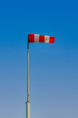 Red and white colored windsock against a bright blue sky. It's a sunny day in the Dutch spring season.