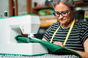 Middle-aged woman sews with the sewing machine at home.