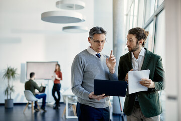Young trainee discussing about data with mature business mentor who is using laptop in the office.