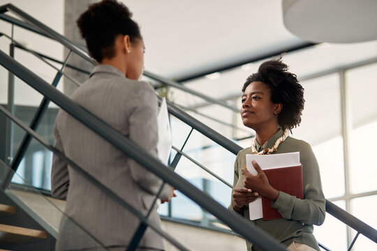 Young black businesswoman talks to her mentor at staircase of office building.