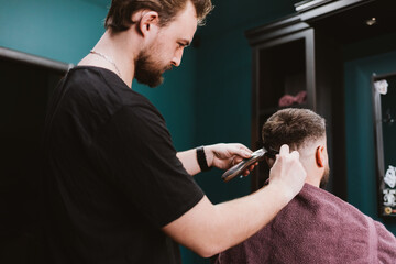 Young male barber doing haircut with clipper