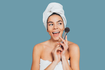 Excited cheerful young woman in bath towel holding makeup brush