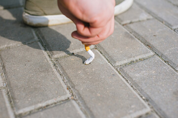 A man puts out a cigarette on the sidewalk tiles.