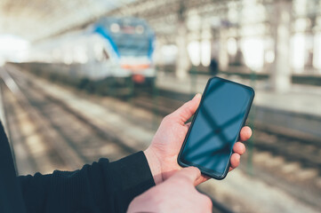 A man holds a mock-up of a smartphone on the background of a train at a railway station.