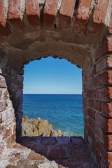 View of the Mediterranean Sea through a small window in the brick wall of the fortress. Antibes, France.