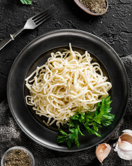 Tasty appetizing classic Italian spaghetti on a plate with parsley and spices over a dark background, top view. Concept of clean eating