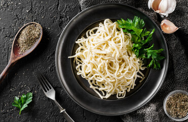Tasty appetizing classic Italian spaghetti on a plate with parsley and spices over a dark background, top view. Concept of clean eating
