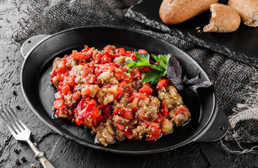 Delicious eggplant salad with pepper and tomatoes on large plate over dark background. Healthy vegan food, clean eating, top view