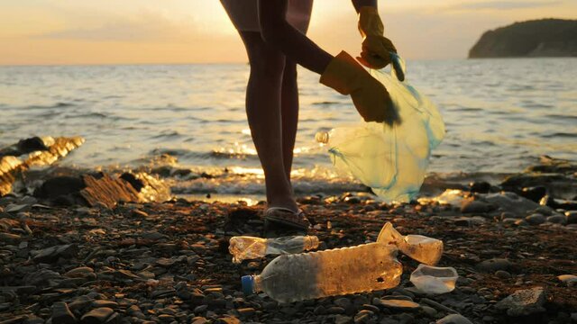 Hand woman in yellow gloves picking up empty plastic bottles cleaning on the beach. Volunteer picking up trash on the sea. Clean planet Earth, collect garbage, avoid pollution. Ecological problem.