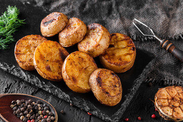 Tasty grilled potatoes with spices on a black rock, dark background, close up view. Barbecue concept food, vegan