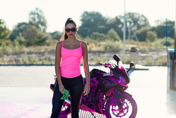 Fototapeta na wymiar Seductive young woman in pink t-shirt poses near sport motorcycle at self service car wash in the morning.