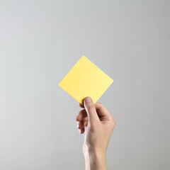 The hand holds an empty square yellow sheet of paper. A clean flyer in your hands. For your text. Isolated on a gray background