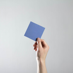 The hand holds an empty square blue sheet of paper. A clean flyer in your hands. For your text. Isolated on a gray background