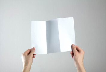 Hands hold a white three fold flyer. A clean flyer in your hands. For your text. Isolated on a gray...