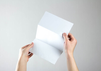 Hands hold a white three fold flyer. A clean flyer in your hands. For your text. Isolated on a gray background
