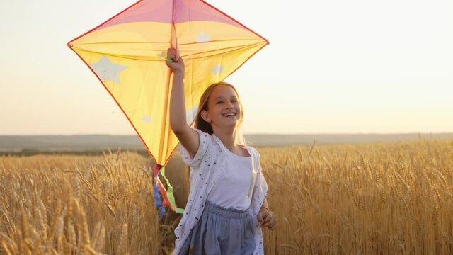 Childhood dream. Happy girl run with a kite in a field of wheat. Child is holding a kite in his hands. Toy in the hands of a girl at sunset. Concept happy family. Freedom of action.
