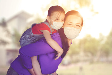Mother in face mask piggybacking her daughter
