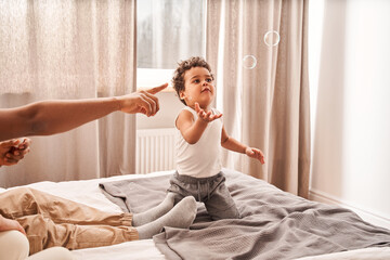 Child looking at the soap bubbles while his parents blowing it