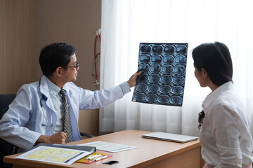 Asian doctor holding x-ray radiography to patient reviewing brain X-ray.