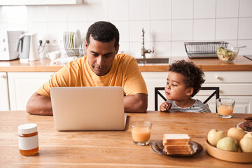 Fototapeta na wymiar Man working t the laptop while his son having breakfast