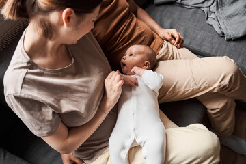Woman looking at her newborn son while sitting at the sofa at the living room