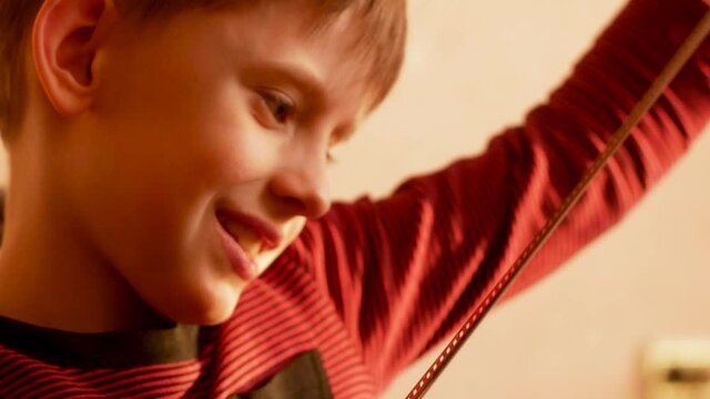 A cheerful Caucasian preschooler child examines a negative old photographic film and experiences positive emotions. The boy keeps family traditions. Nice memories on film. Selective focus, shallow dep