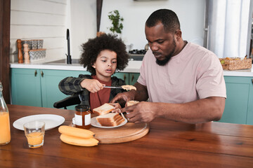 Boy spreads peanut butter to toast while having breakfast