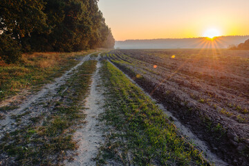 Beautiful sunrise on a country road along a plowed field.