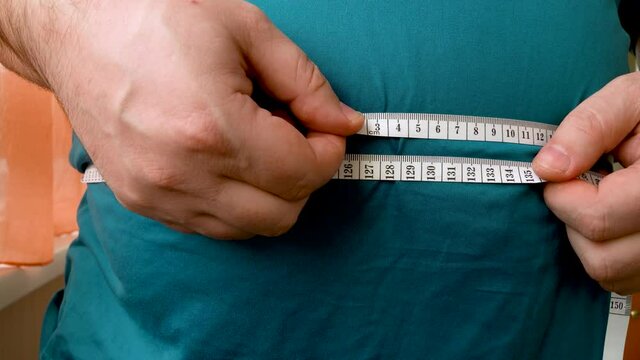 man measures the size of the abdomen with a centimeter measuring tape. Fat man gained or lost weight. fatty person controls body weight. problems of obesity