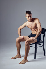Fototapeta premium sporty man with a pumped up body in black shorts sits on a chair isolated background