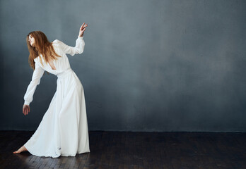 Fototapeta na wymiar A woman in a white dress is dancing on a gray background in full growth red hair model