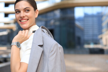 Smiling business woman standing with a jacket over her shoulder near office building.