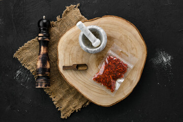 Wooden cross section with crushed paprika in plastic package and mortar and mill