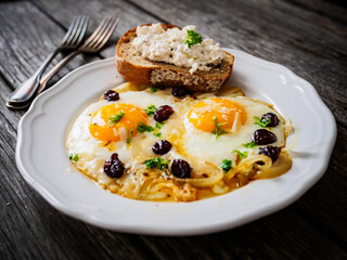 Continental breakfast - sunny side up eggs with onion and parmesan on wooden background