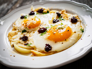 Continental breakfast - sunny side up eggs with onion and parmesan on wooden background