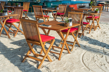Wooden table and chairs in empty beach cafe next to sea water. Close up, Thailand
