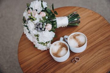 Wedding morning. A wedding bouquet, two cups of coffee and wedding rings lie on the table. aesthetics and details of the wedding - 421981922